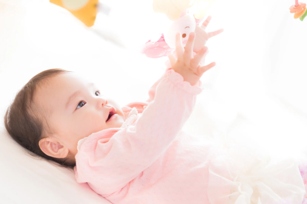 ベッドに寝転がっておもちゃに手を伸ばす赤ちゃん