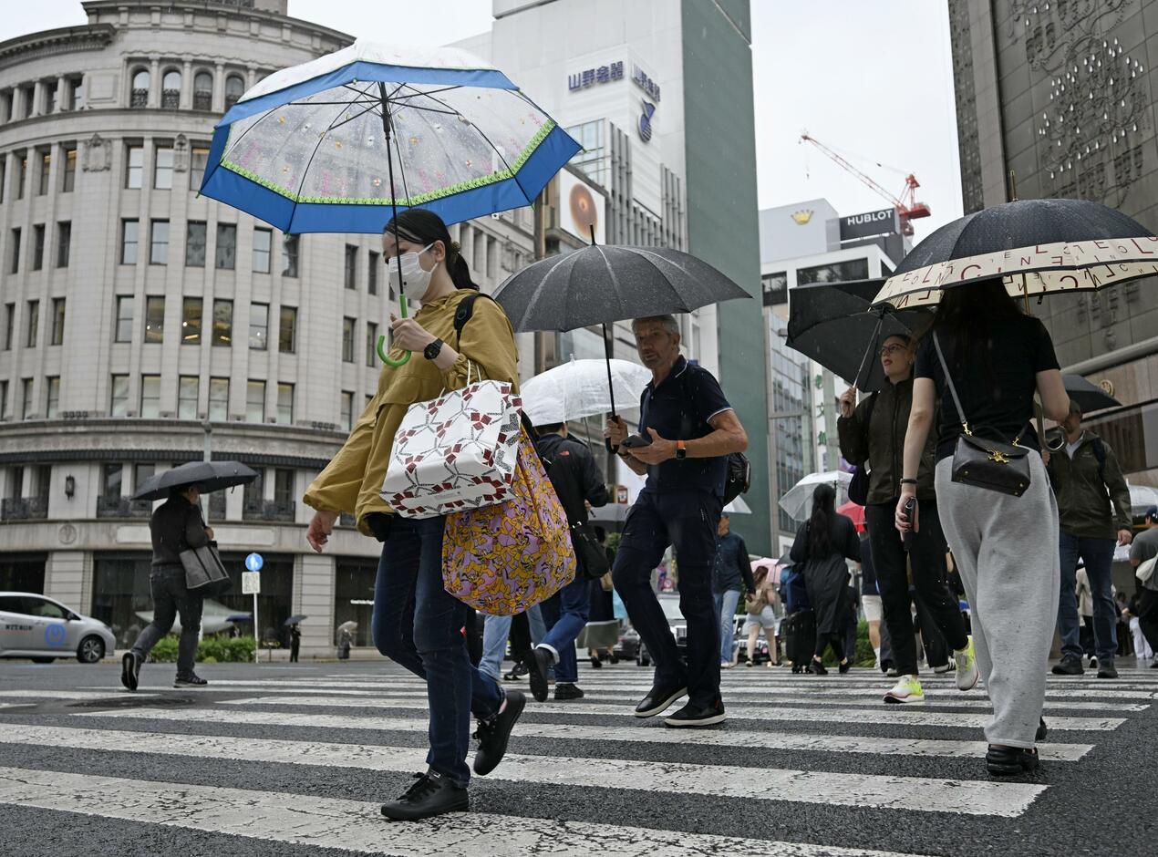 東京・銀座の街角で傘を差して横断歩道を渡る人々
